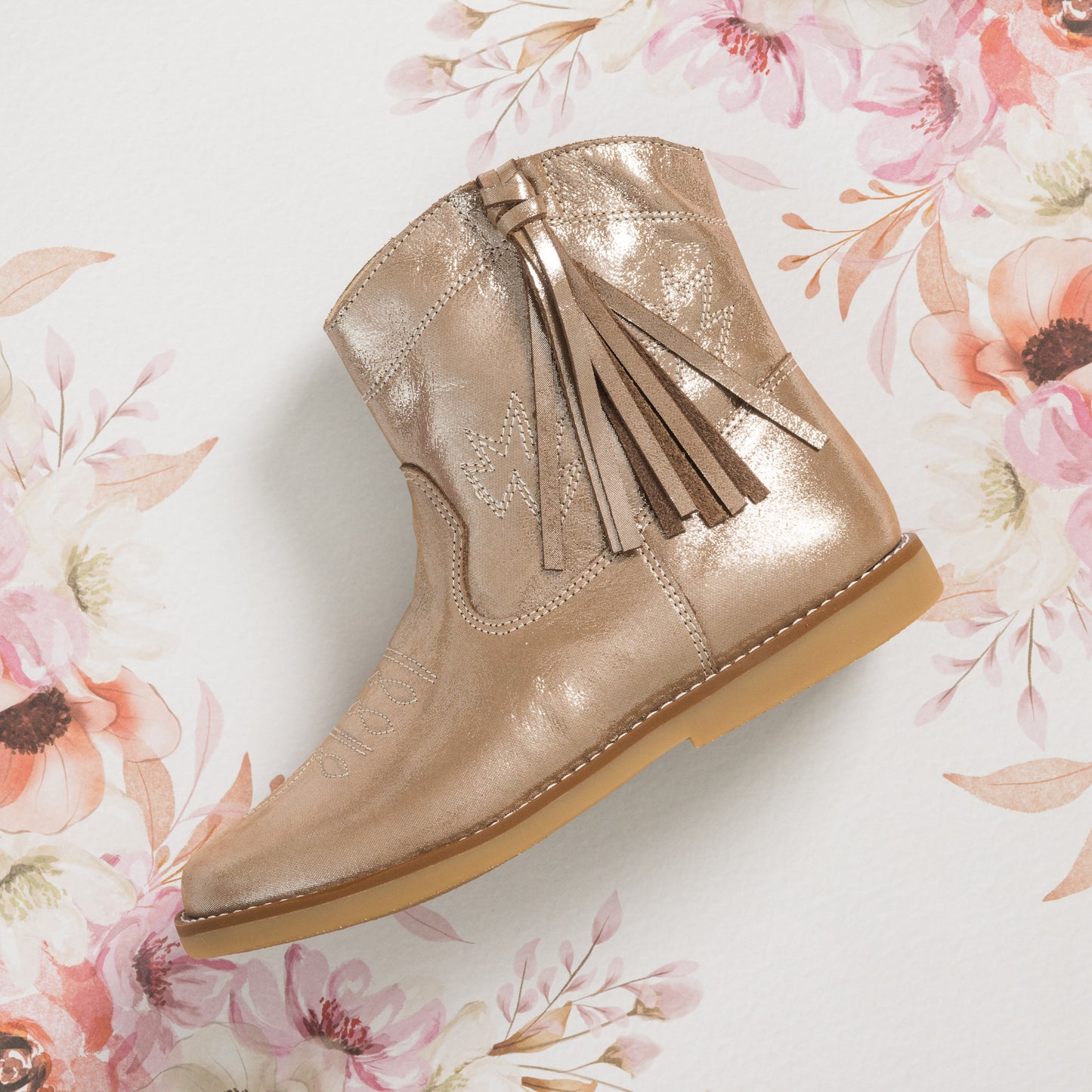 Metallic blush suede toddler boot with side tassel and light brown sole on floral background.