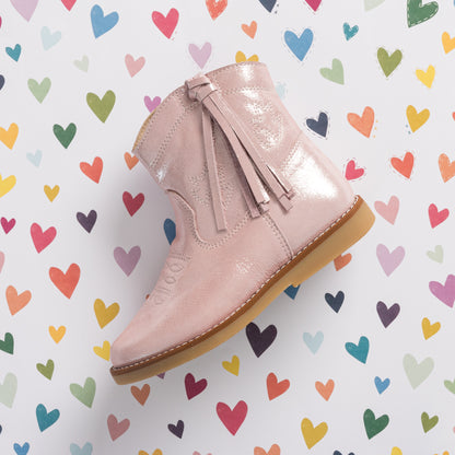 Metallic pink suede toddler boot with tassel zipper and light brown sole against colorful heart background.