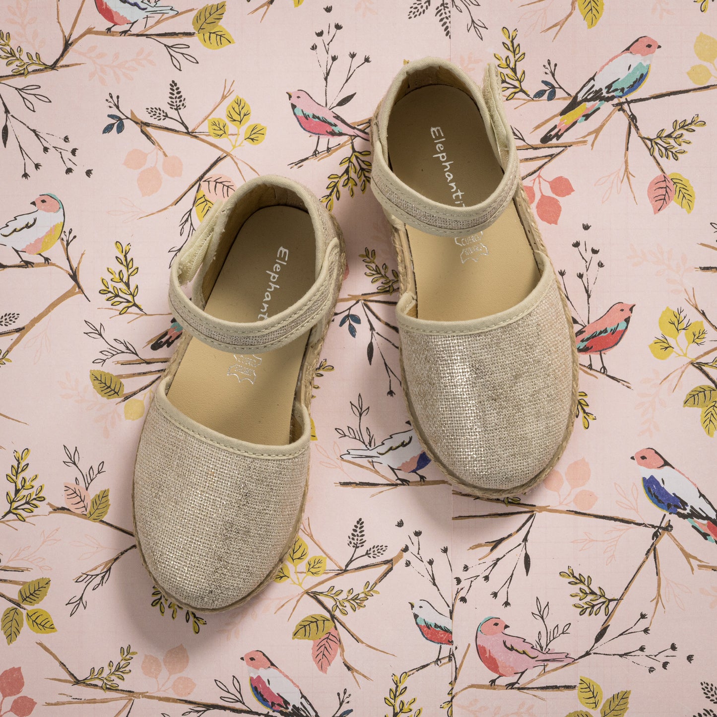Metallic white linen espadrille with ankle strap and braided jute sole on floral background.