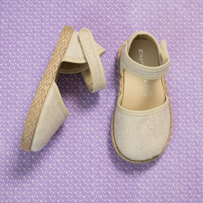 Metallic white linen espadrille for girls with ankle strap and braided jute sole on purple patterned background.