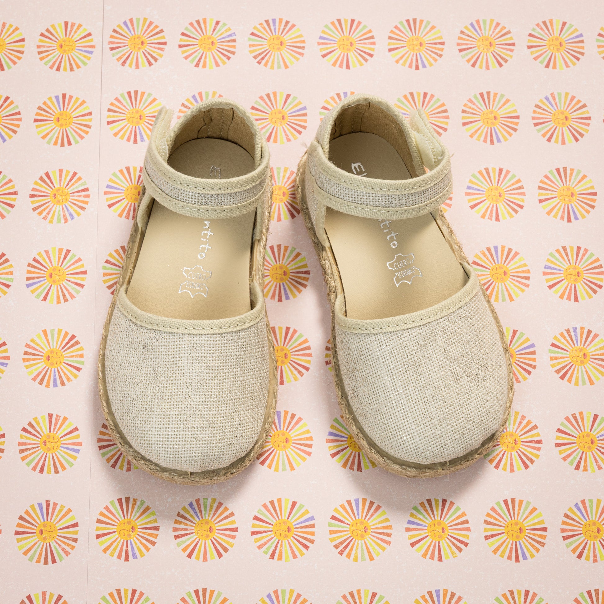 Metallic white linen toddler espadrille sandals with ankle strap and rounded toes on patterned background.