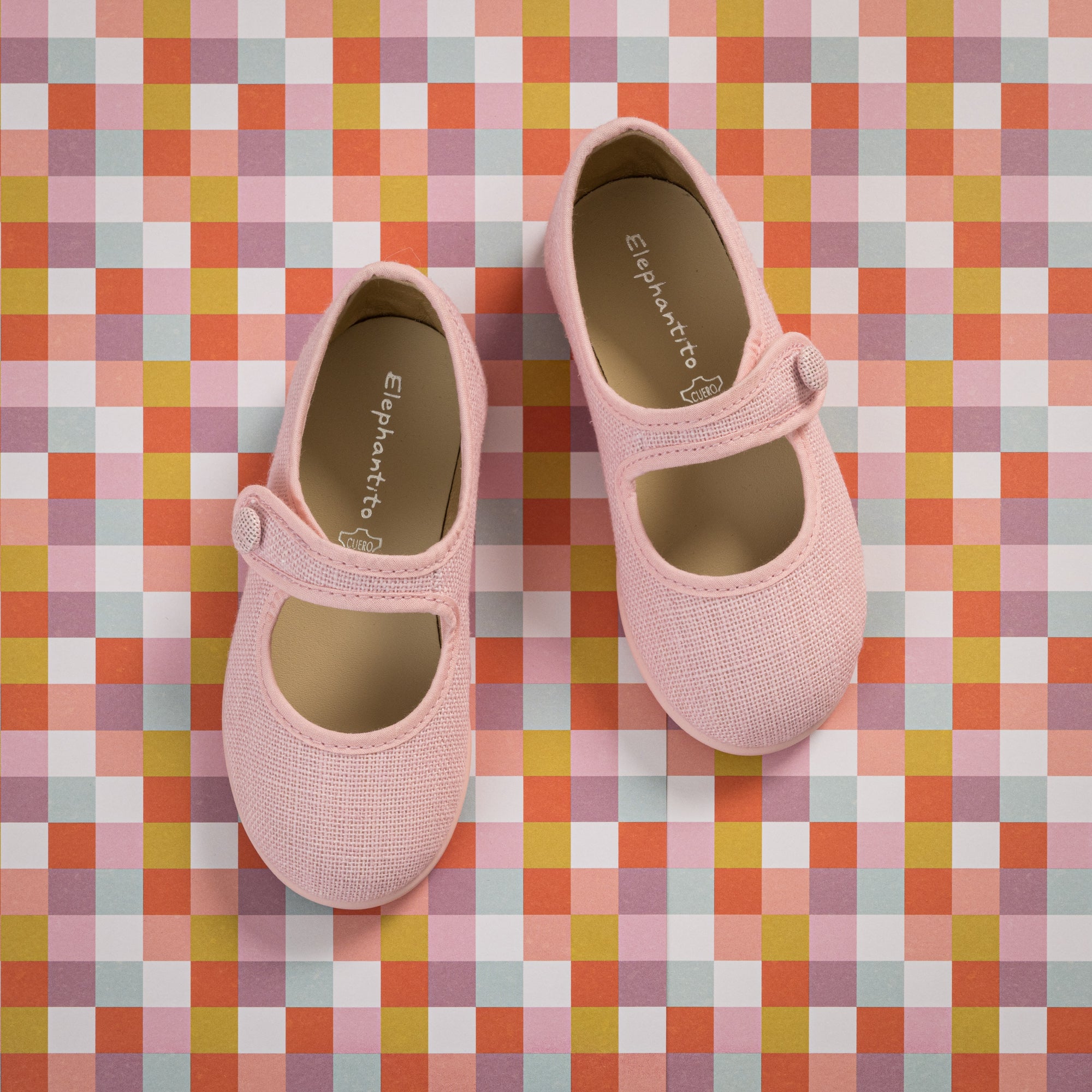 Pink linen Mary Jane shoes for toddlers with a single strap and round toe on a colorful checkered background.