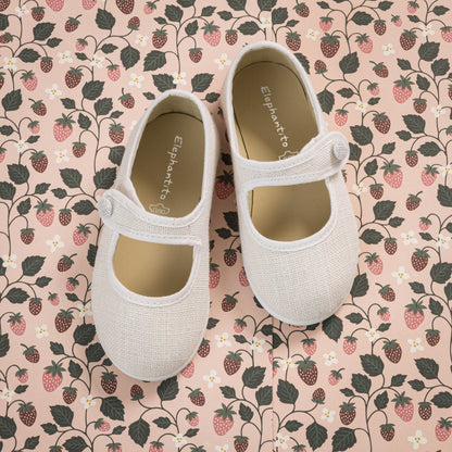 White linen Mary Jane toddler shoes with adjustable strap on floral fabric background.