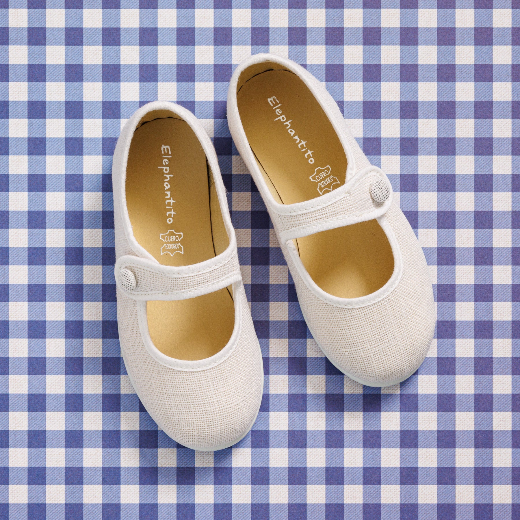 Elephantito - White linen Mary Jane shoes for girls with button strap and rounded toe on blue checkered background.