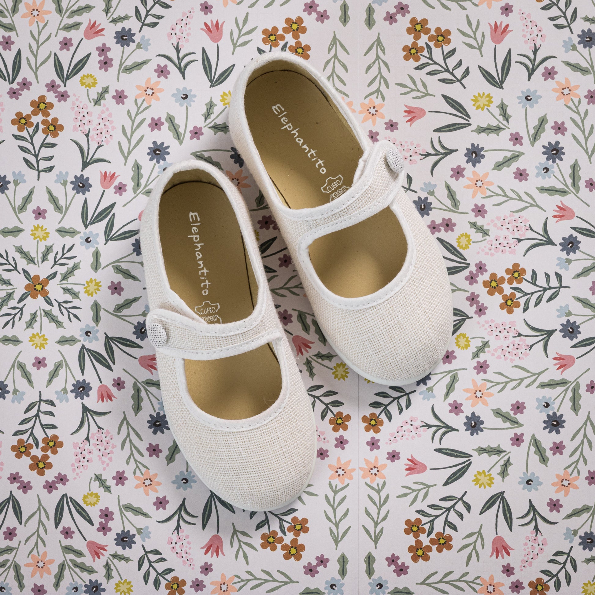 White linen Mary Jane toddler shoes with single strap and round toe on floral background.