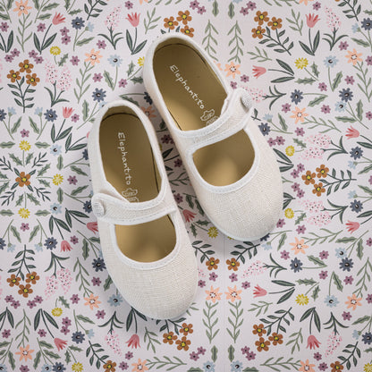 White linen Mary Jane toddler shoes with single strap and round toe on floral background.
