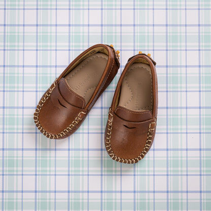 Natural brown toddler moccasin shoes with stitched detailing and penny loafer style on plaid background.