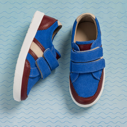 Blue denim boys sneakers with brown leather accents and double velcro straps on white soles.