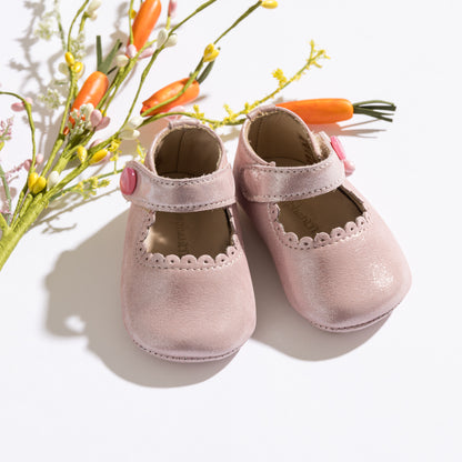 Soft pink baby Mary Jane shoes with scalloped edges and buttoned straps on white background.