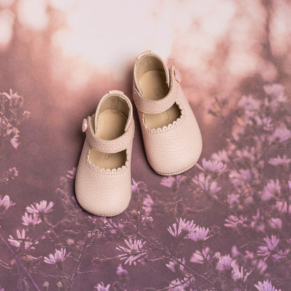 Soft pink baby Mary Jane shoes with scalloped edges and a single strap buckle closure.