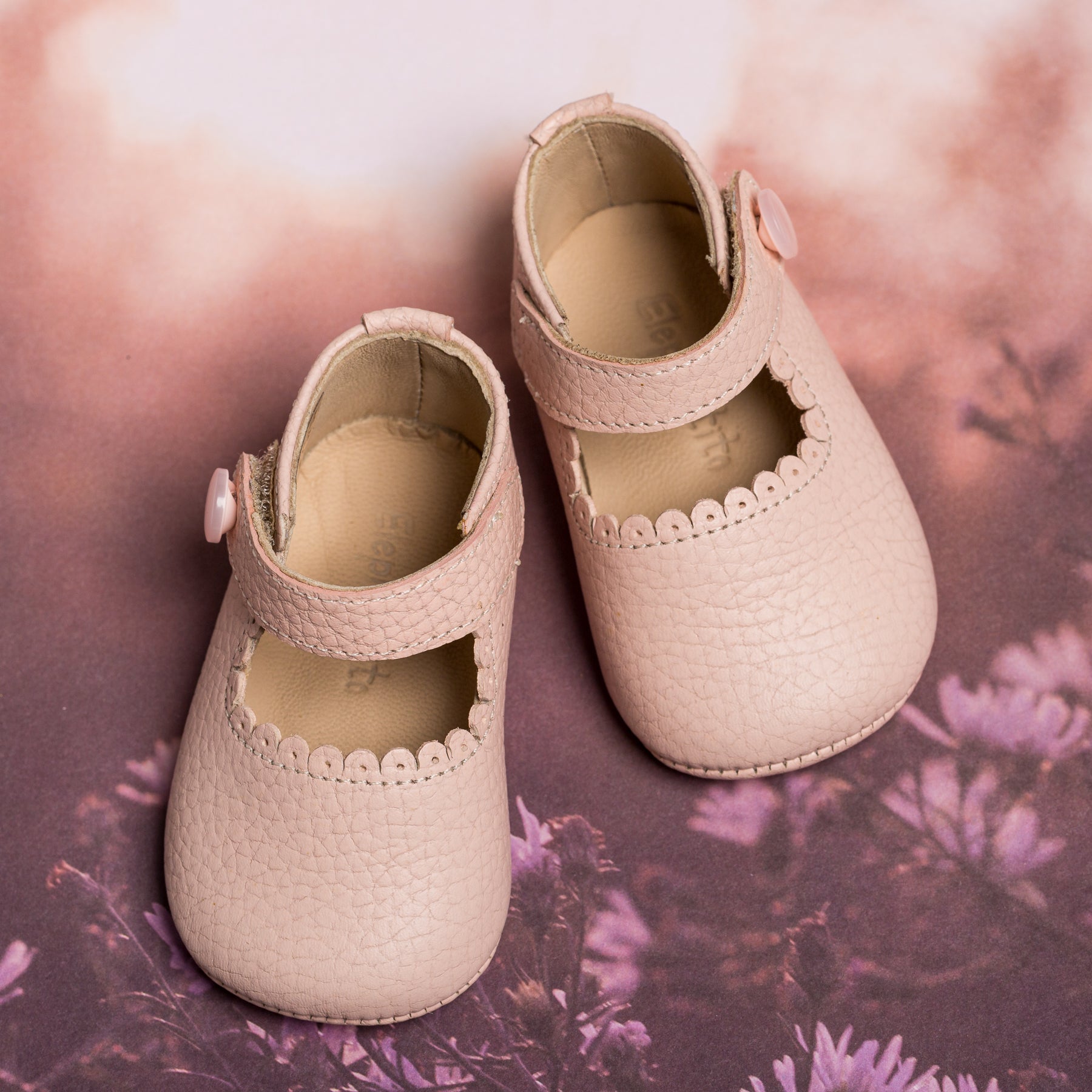 Soft pink textured leather baby Mary Jane shoes with scalloped edge and side button strap.