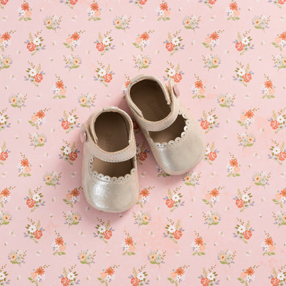 Talc-colored baby Mary Jane shoes with scalloped edges on a pink floral background.