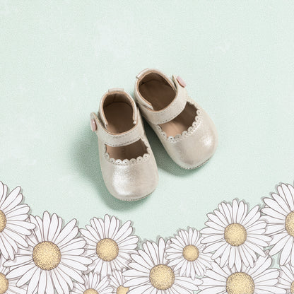 Soft pink baby Mary Jane shoes with scalloped edges and a velcro strap on a light green background.