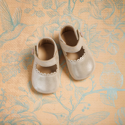 Soft beige toddler Mary Jane shoes with scalloped edges and Velcro straps on patterned fabric background.
