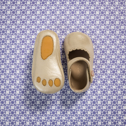 Soft cream-colored baby Mary Jane shoes with scalloped edges and a tan sole patch shaped like toes.