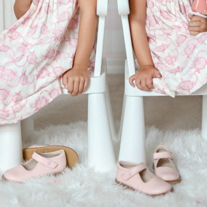 Pair of light pink Mary Jane shoes with a strap and buckle detail on white fluffy rug.