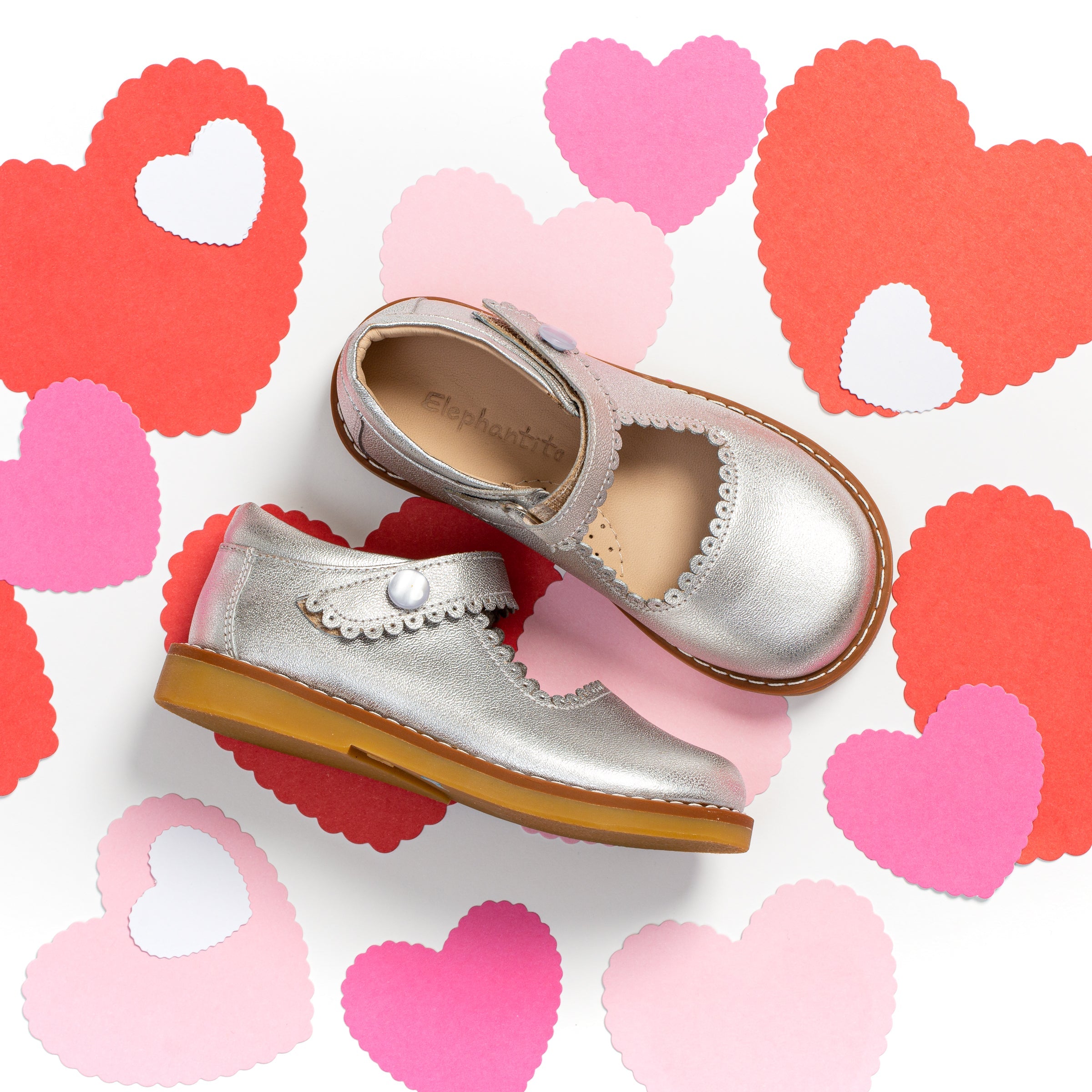 Silver leather Mary Jane shoes for girls with scalloped edges and pearl button straps on tan soles.