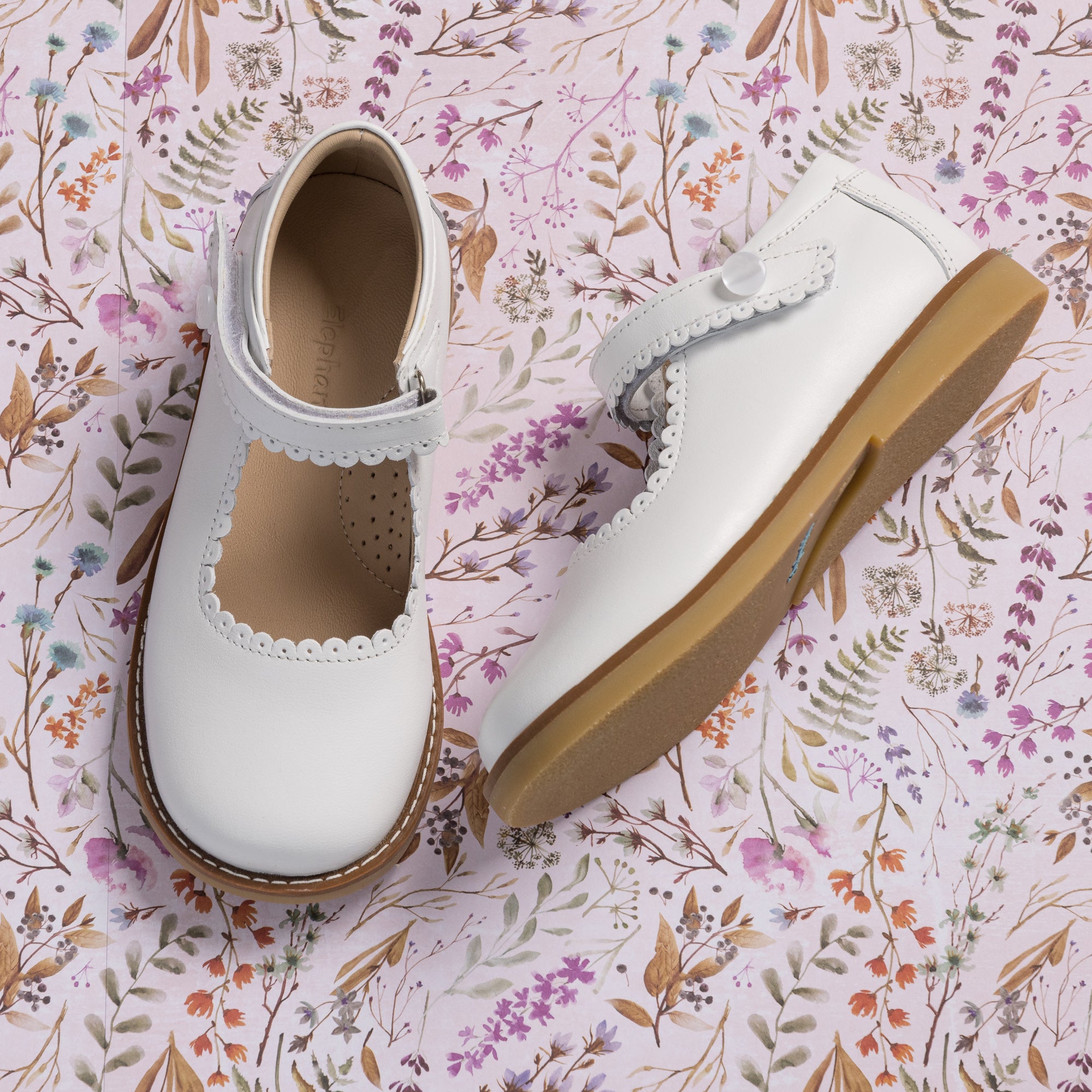 White leather Mary Jane shoes with scalloped edges and velcro strap, tan rubber sole.