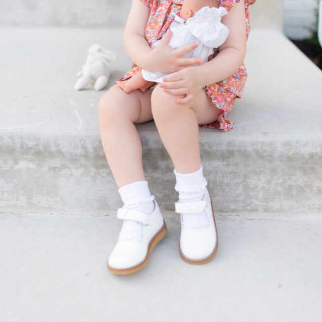 White leather toddler Mary Jane shoes with double straps and beige soles worn with white socks.