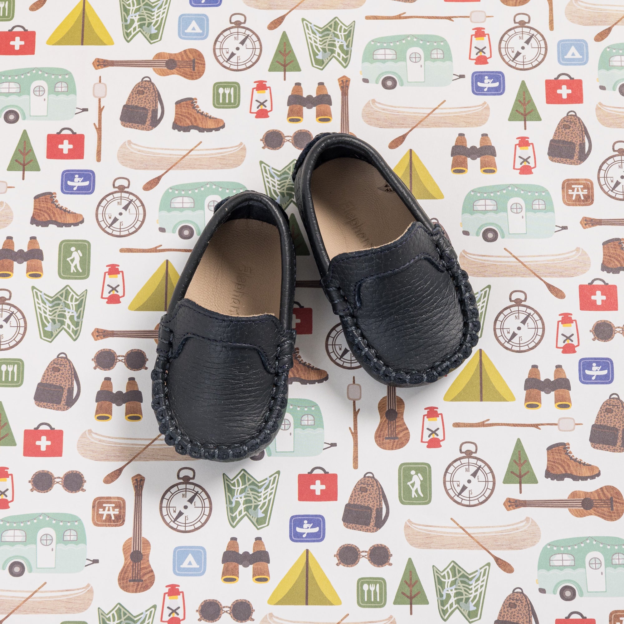Navy blue baby moccasins with stitched detailing and soft leather lining on patterned background.
