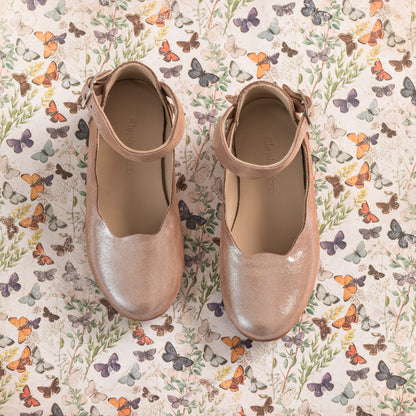 Blush pink toddler ballerina flats with ankle straps on butterfly print background.