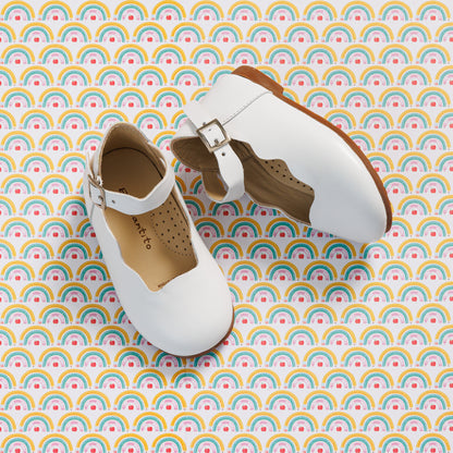 Elephantito - White toddler Mary Jane flats with buckle strap and perforated tan interior lining on rainbow-patterned background.