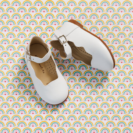 Elephantito - White toddler Mary Jane flats with buckle strap and perforated tan interior lining on rainbow-patterned background.