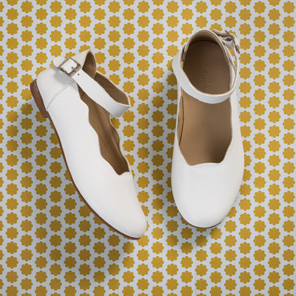 White kids' leather ballerina flats with scalloped edges and ankle strap buckle.