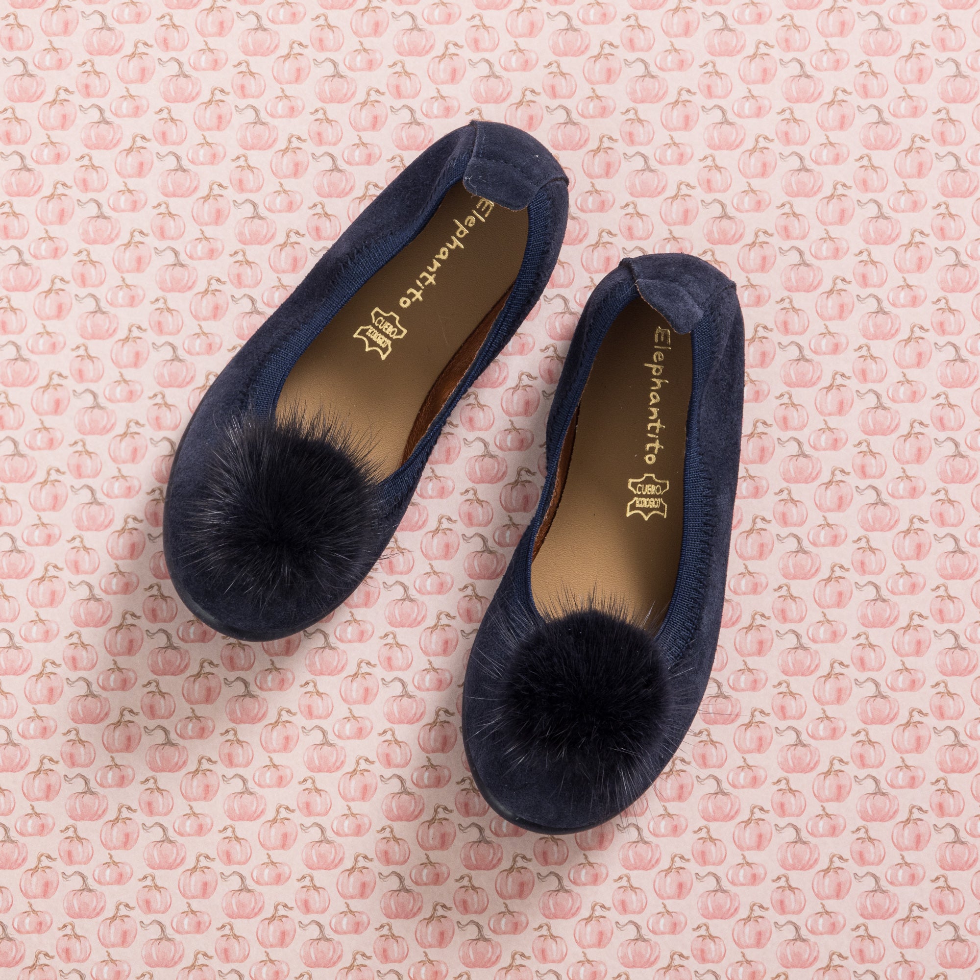 Navy blue suede ballerina flats with large matching pom poms on top and elasticized edges.
