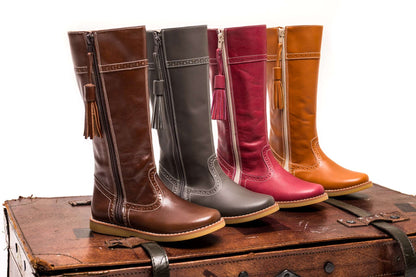 Four tall children's riding boots in brown, gray, red, and tan leather with side zippers and tassel accents, displayed on a.