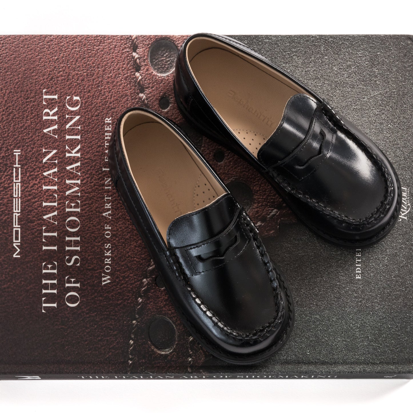 Black leather moccasin loafers for boys with stitched detailing and a penny strap design.