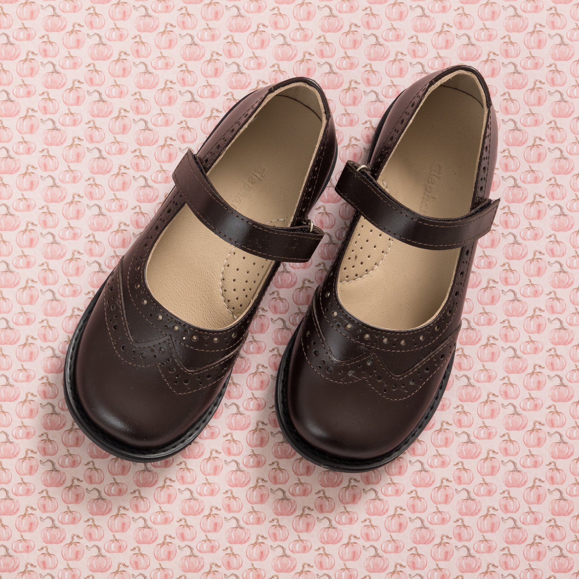 Brown leather Mary Jane shoes for girls with decorative perforations and adjustable straps.
