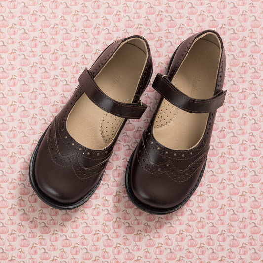 Brown leather Mary Jane shoes for girls with decorative perforations and adjustable straps.