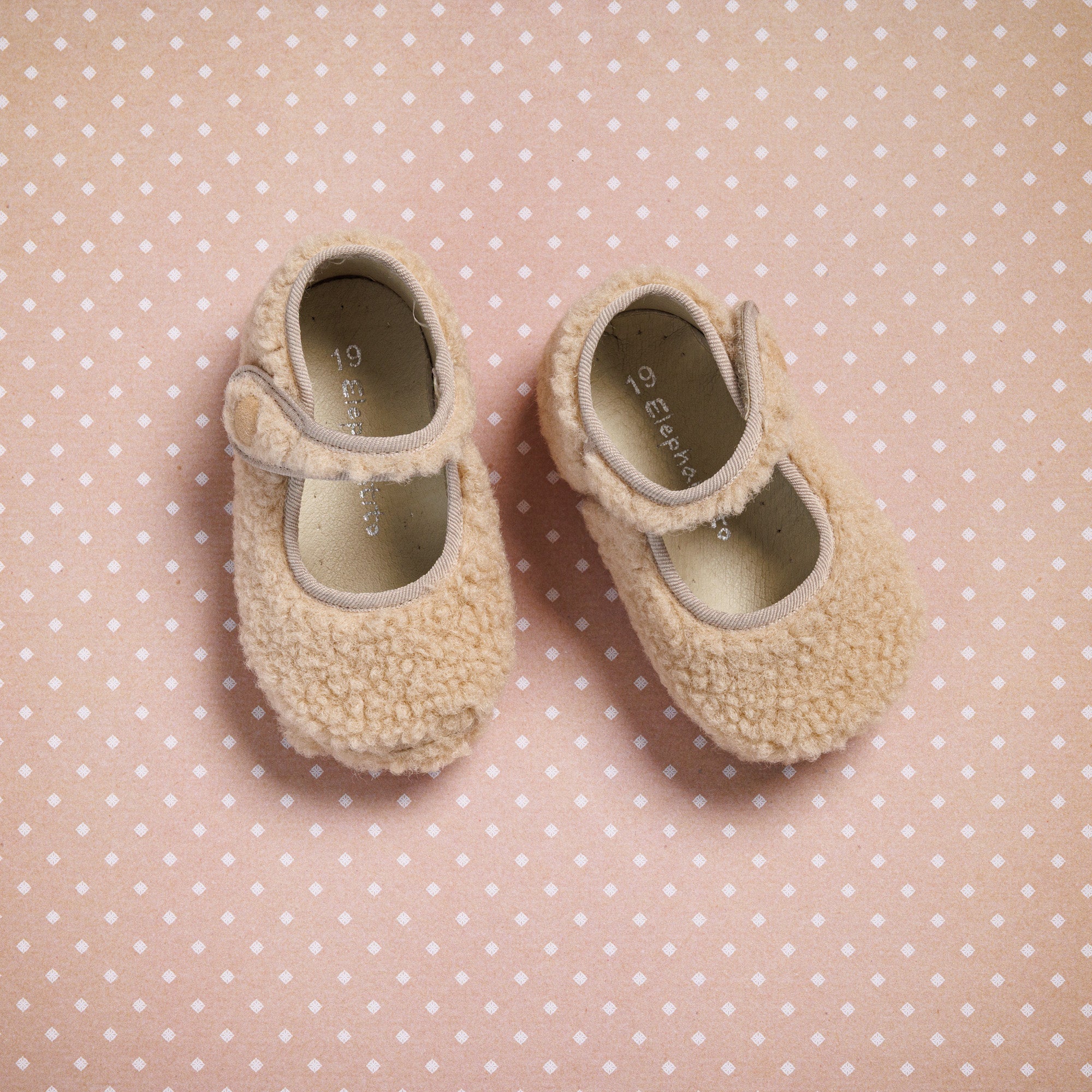 Beige shearling baby Mary Jane shoes with Velcro straps on pink polka dot background.