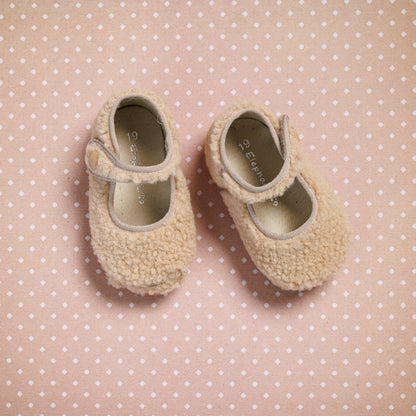 Beige shearling baby Mary Jane shoes with Velcro straps on pink polka dot background.