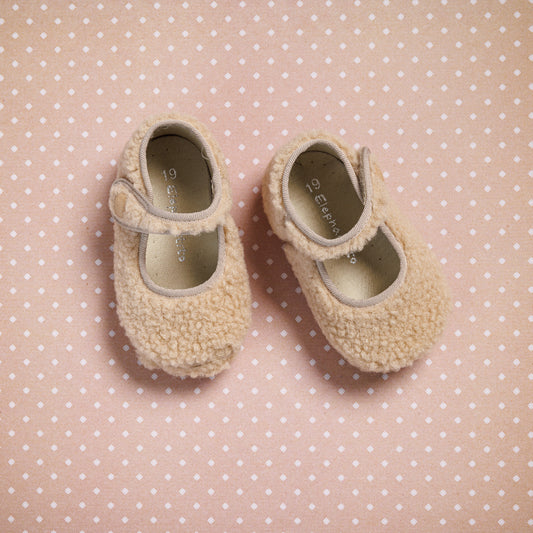Beige shearling baby Mary Jane shoes with Velcro straps on pink polka dot background.