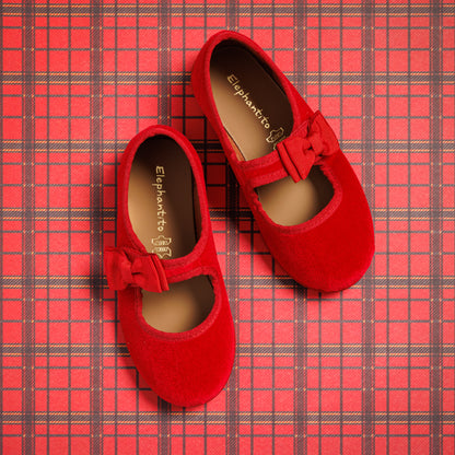 Red velvet Mary Jane shoes with a bow strap on a red plaid background.