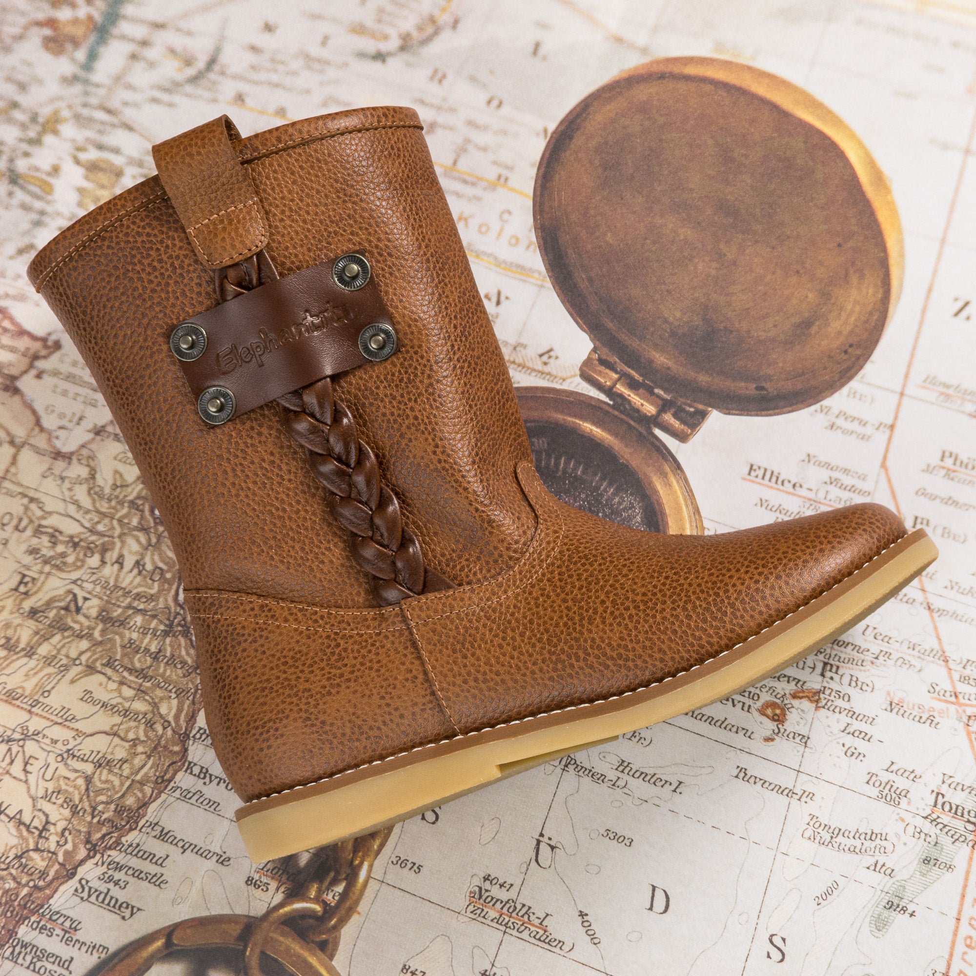 Brown textured leather toddler boot with braided strap and decorative metal studs.