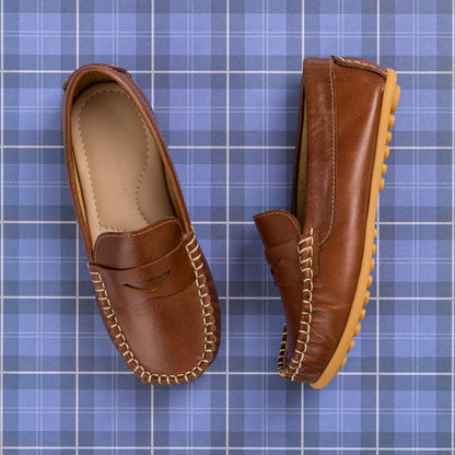 Natural brown leather boys loafer with moccasin stitching and tan rubber sole on blue plaid background.