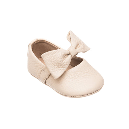 Cream-colored baby ballerina shoe with textured bow and soft sole.