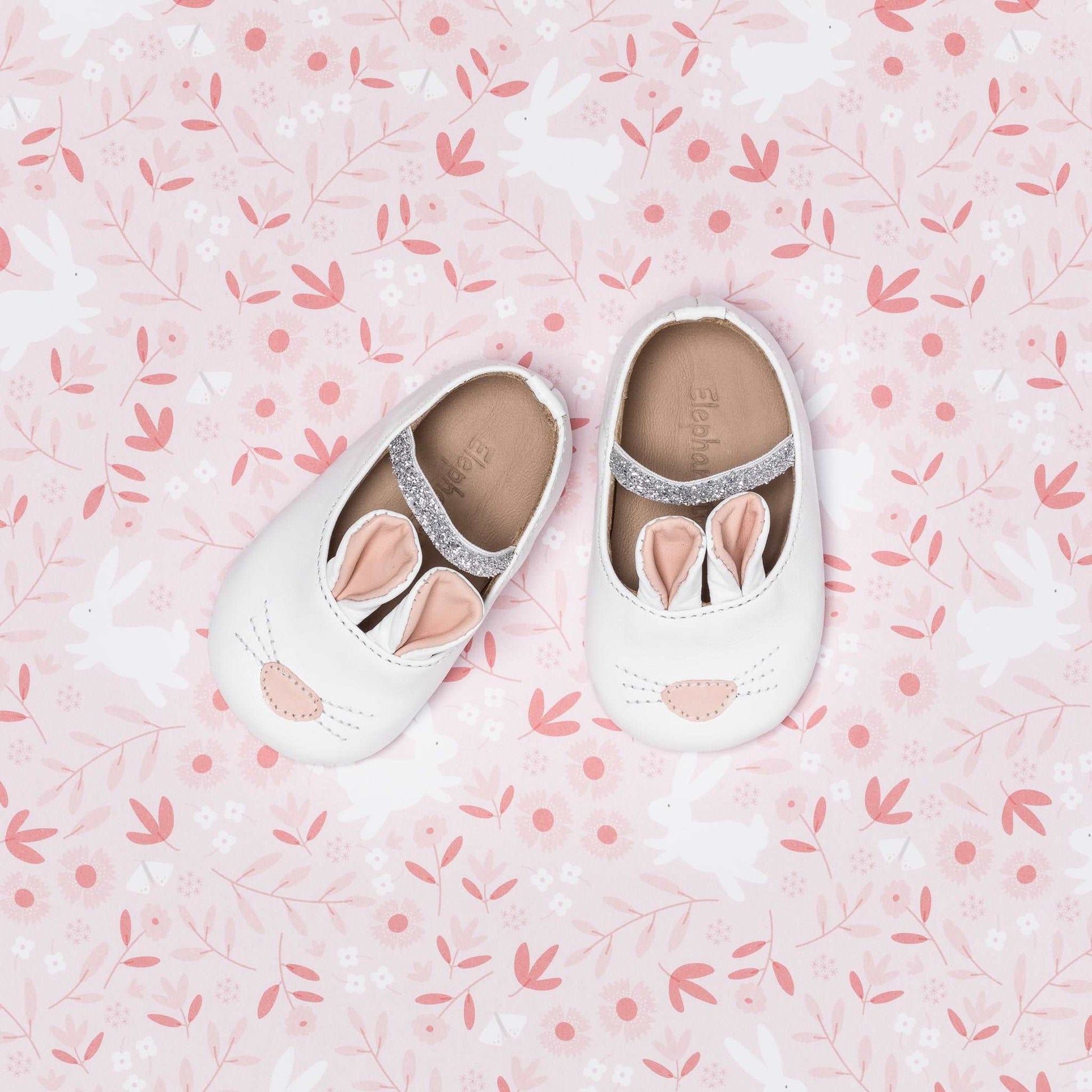 White baby slippers designed as bunnies with pink ears and a small nose detail.