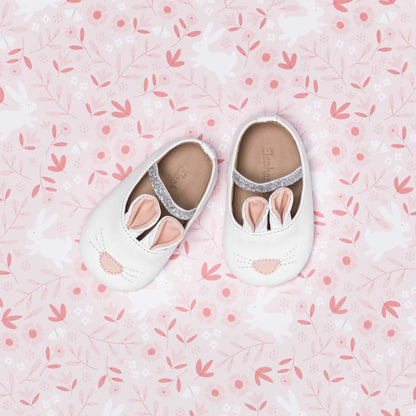 White baby slippers designed as bunnies with pink ears and a small nose detail.