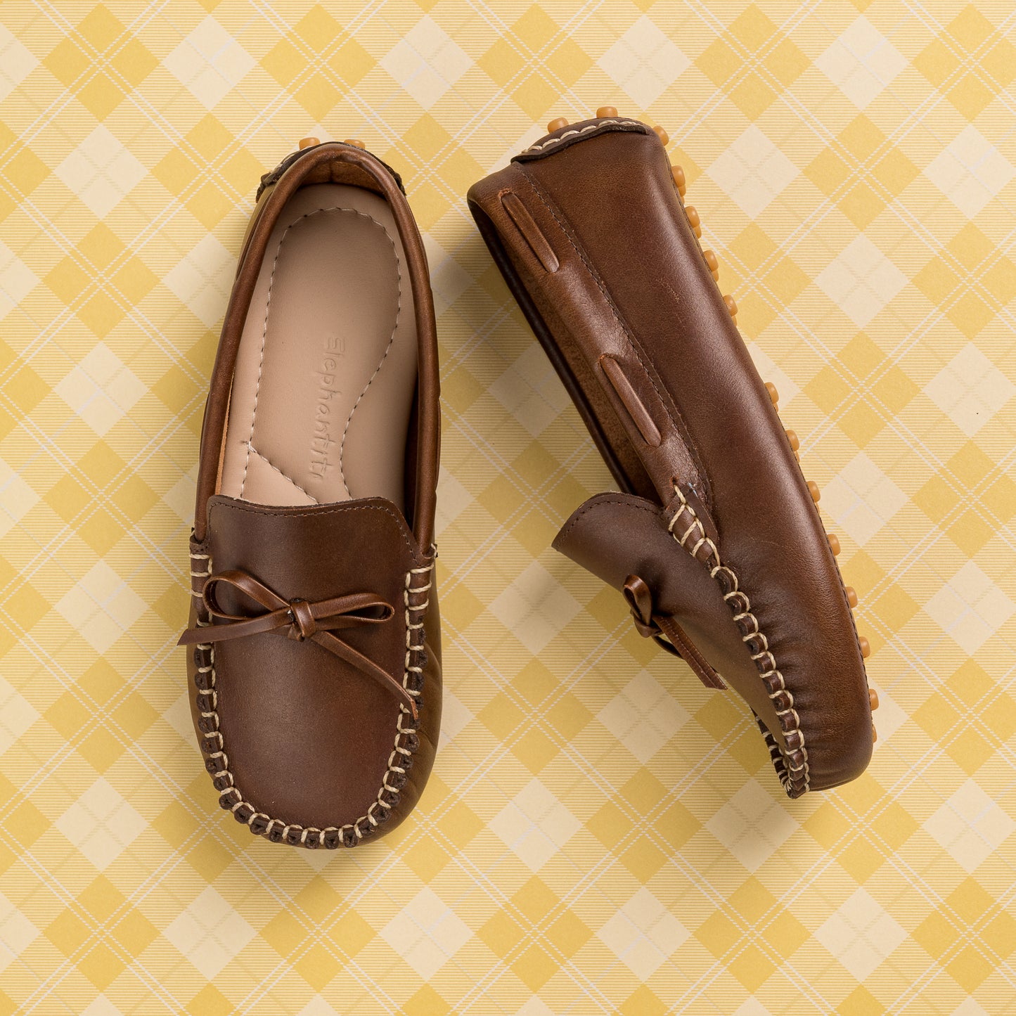 Brown leather boys' driver loafers with moccasin stitching and bow detail on top.
