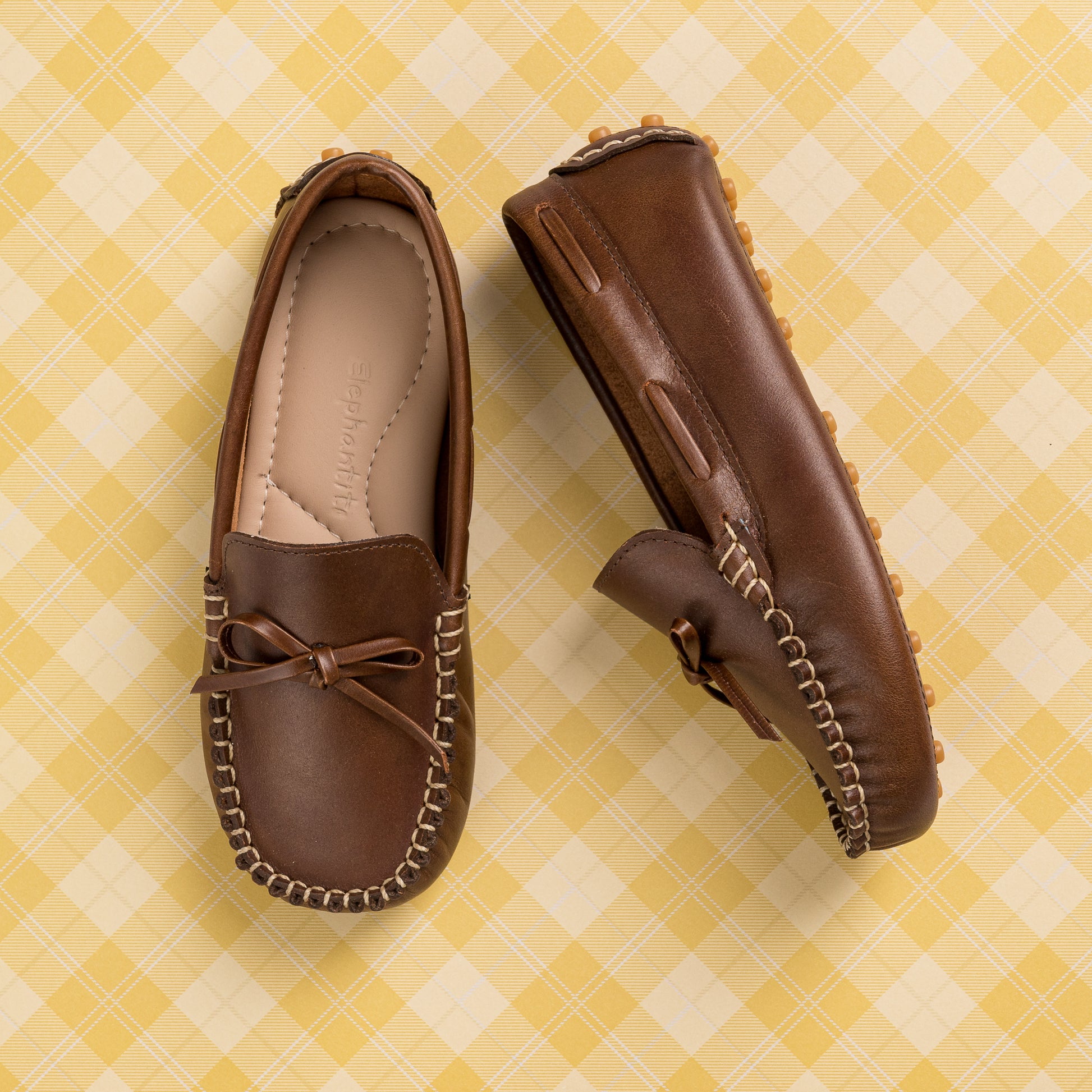 Brown leather boys' driver loafers with moccasin stitching and bow detail on top.