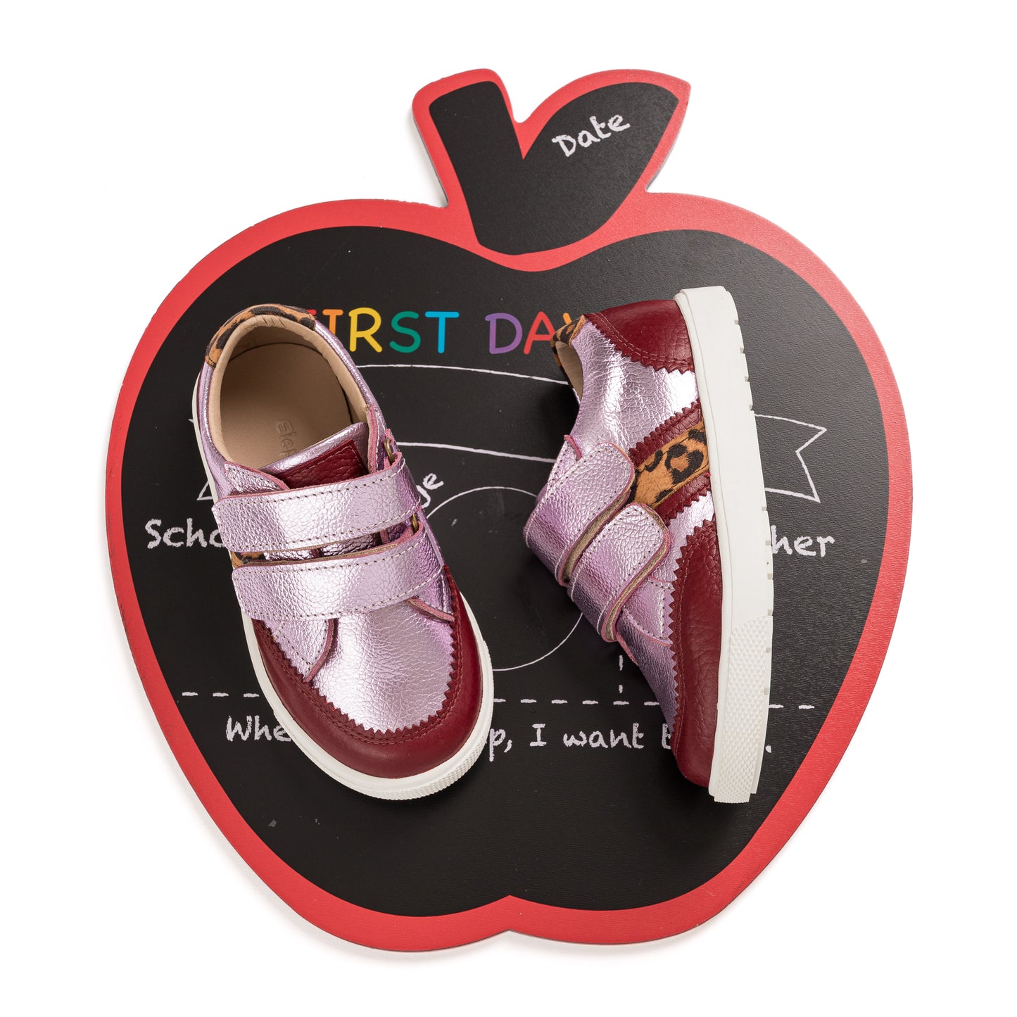 Metallic carnation pink girls' sneakers with velcro straps and white soles on red apple-shaped chalkboard background.