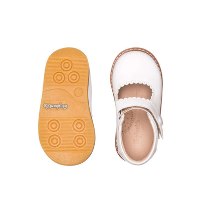 White toddler Mary Jane shoe with scalloped edge and tan rubber sole with circular grips.