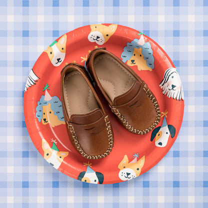Natural brown baby moccasins with stitched detailing on a red plate featuring cartoon dogs.